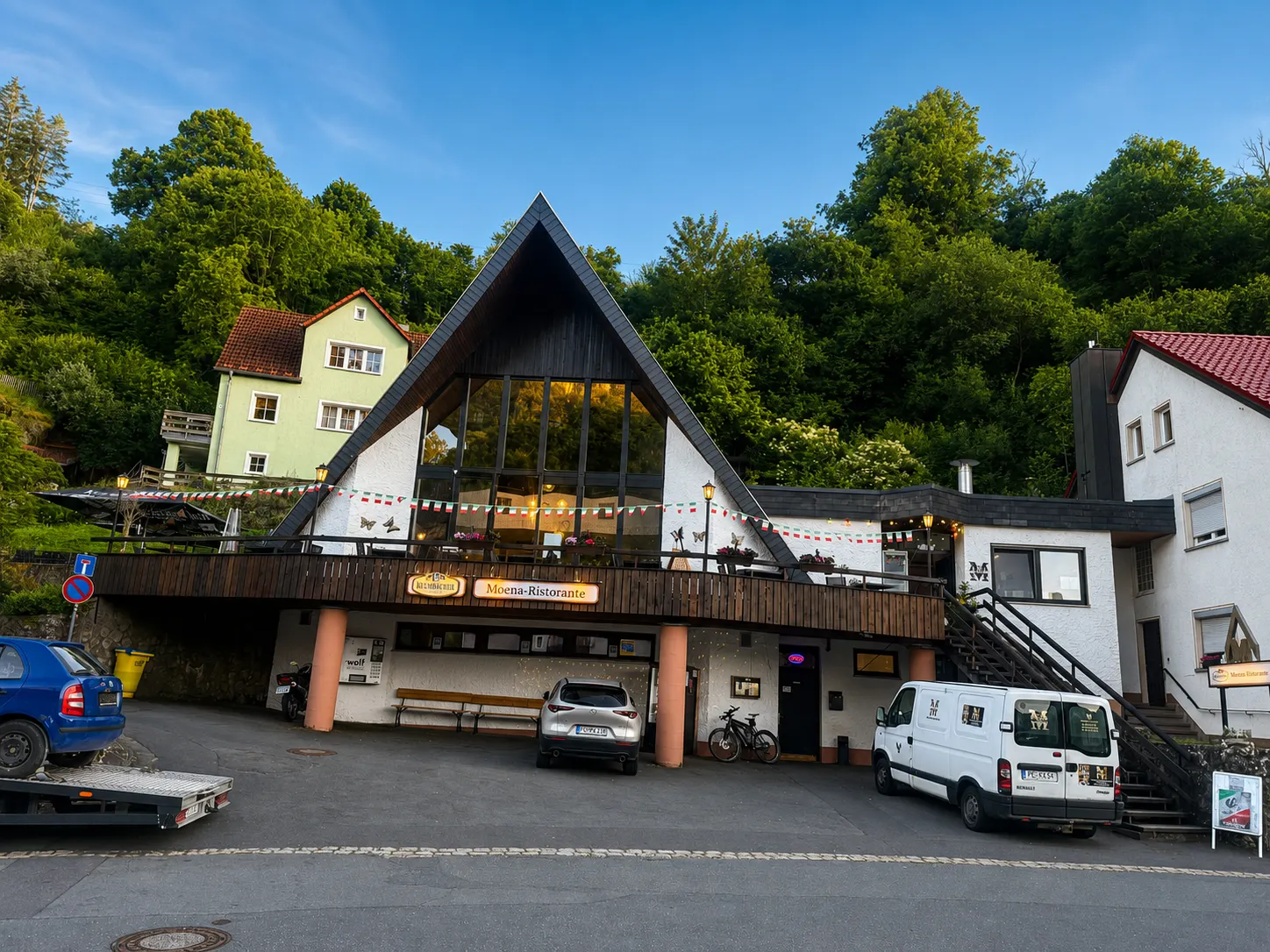 Außenansicht des Restaurant Moena mit blauem Himmel und grünem Hang