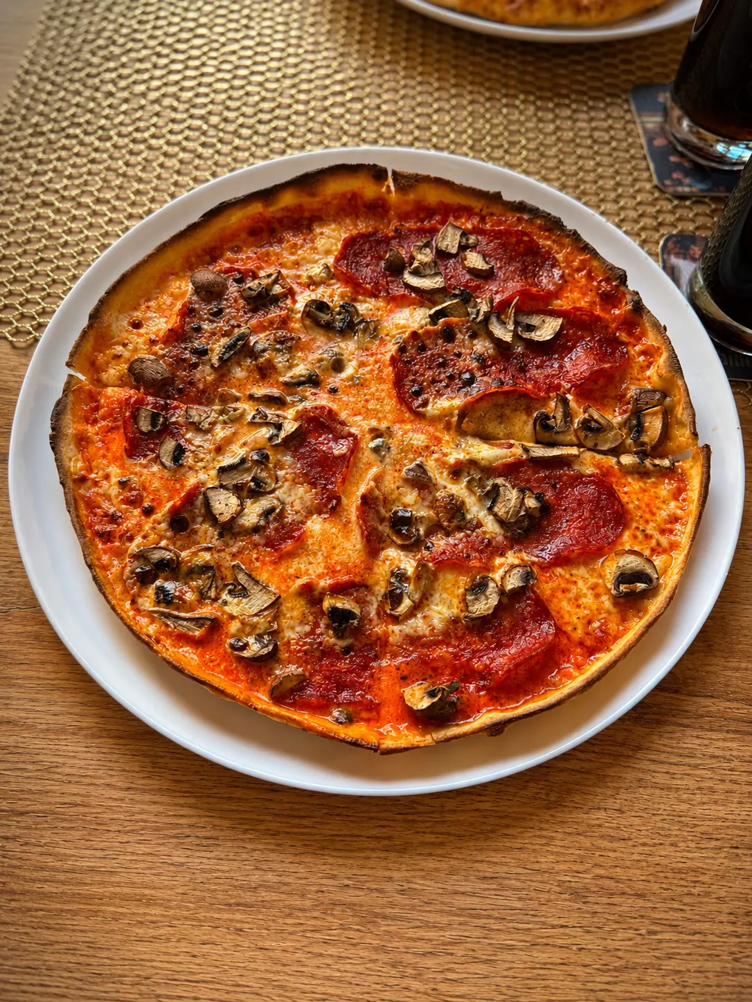 Pizza mit Salami und frischen Champignons auf goldenem Platzset